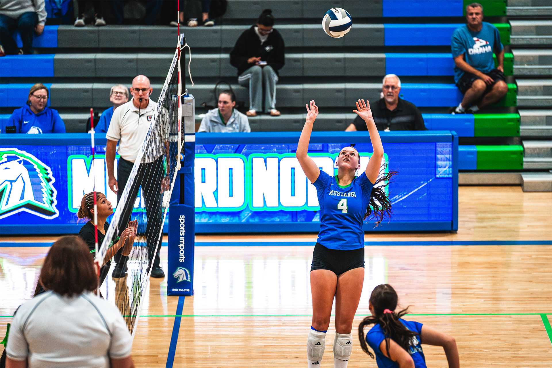A Mustangs setter tracks the ball as the ScoreVision LED scorer’s table energizes the court.