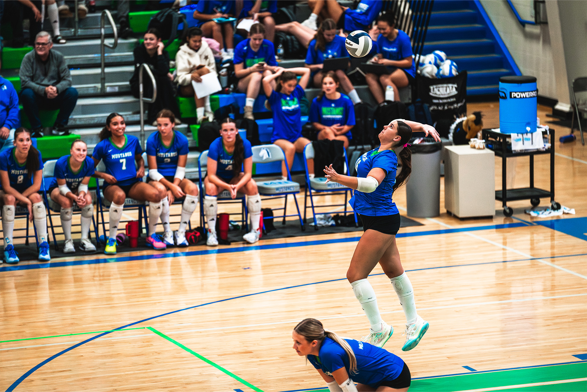 A Millard North server takes flight as her teammates watch from the bench.