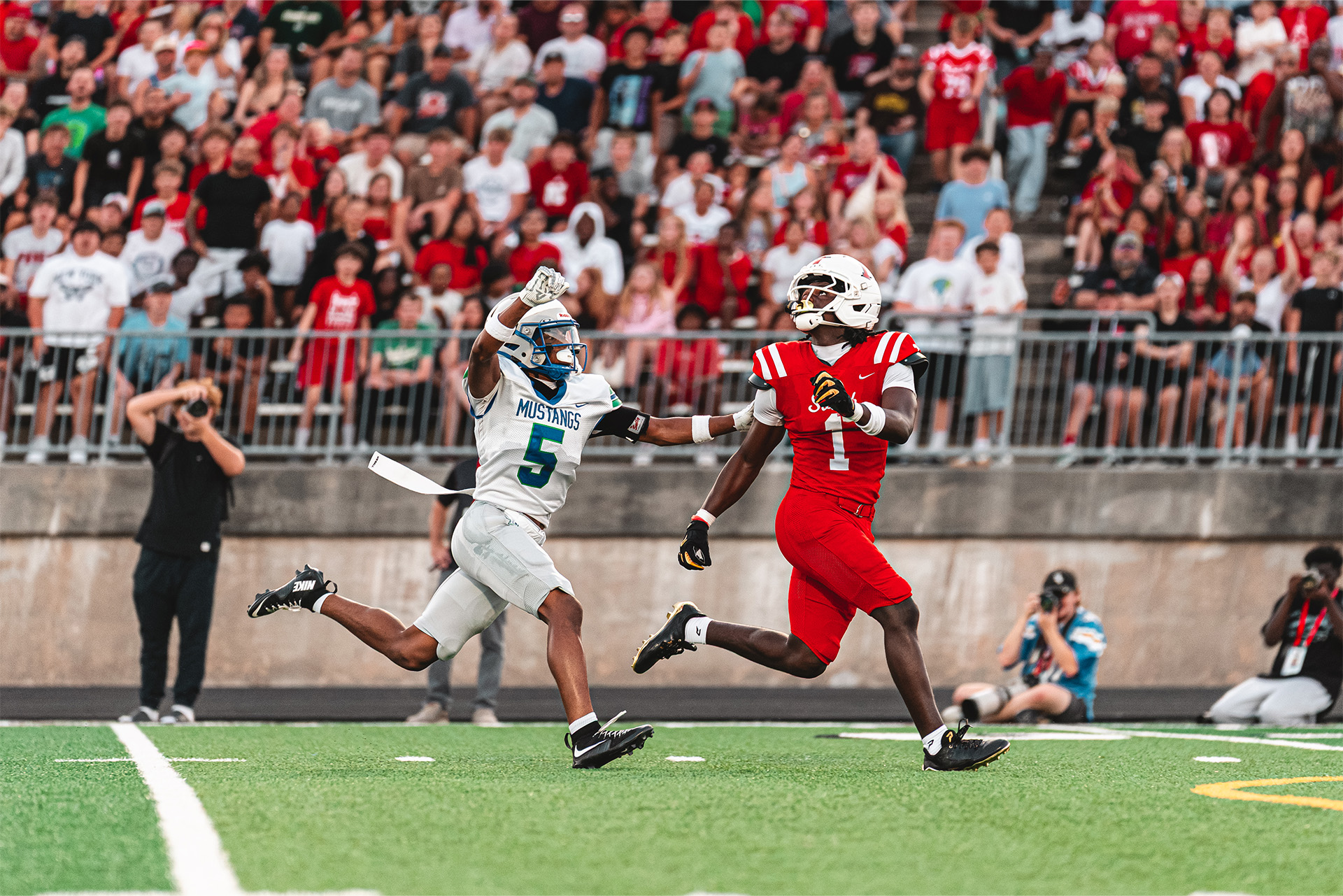 A Patriots receiver tracks the deep ball with a Mustangs defender in pursuit.