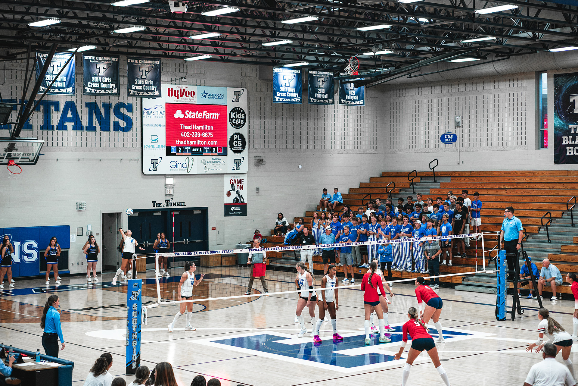 A packed student section looks on as the Titans serve beneath the ScoreVision display.