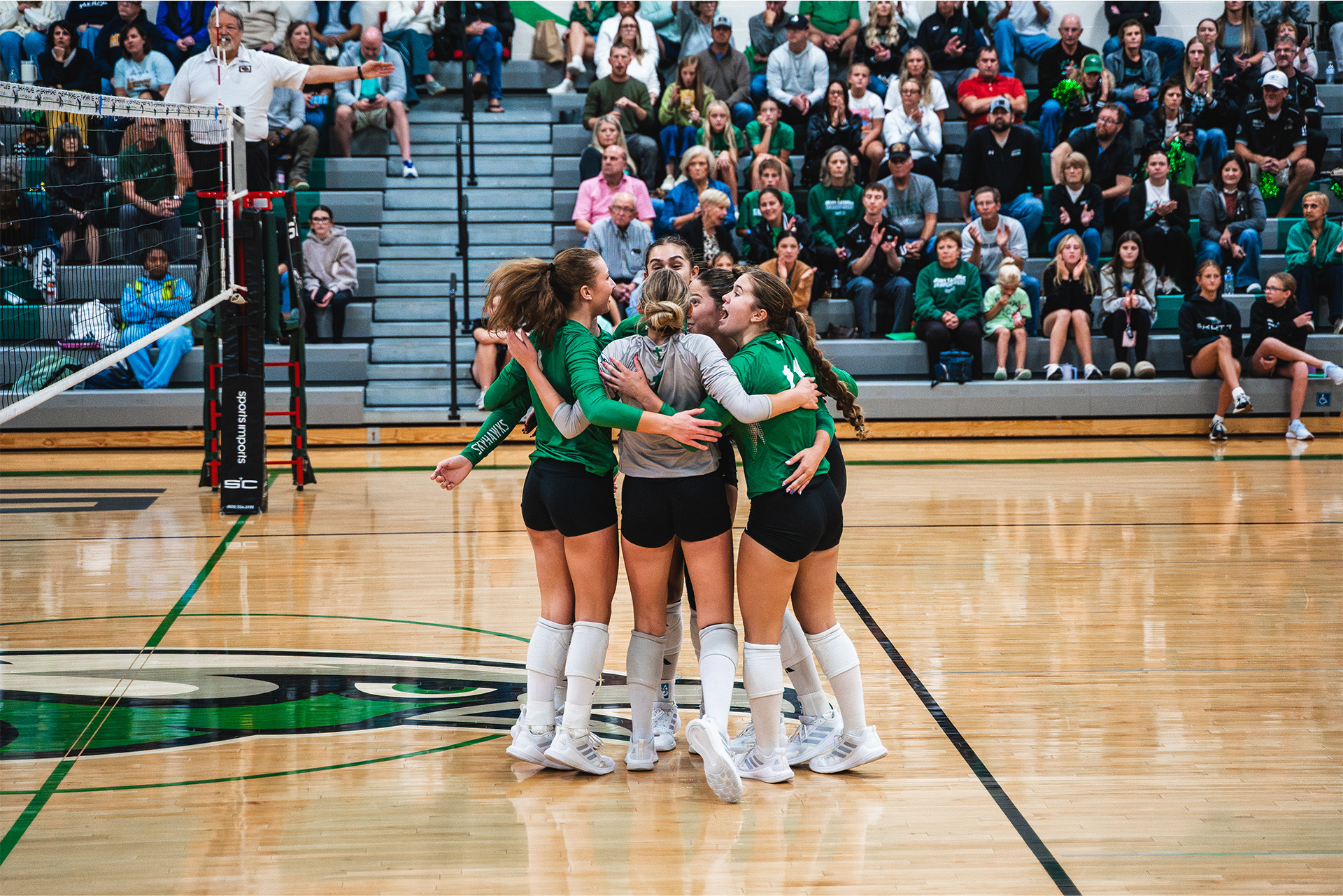 Skutt Catholic volleyball players gather in a celebratory huddle.