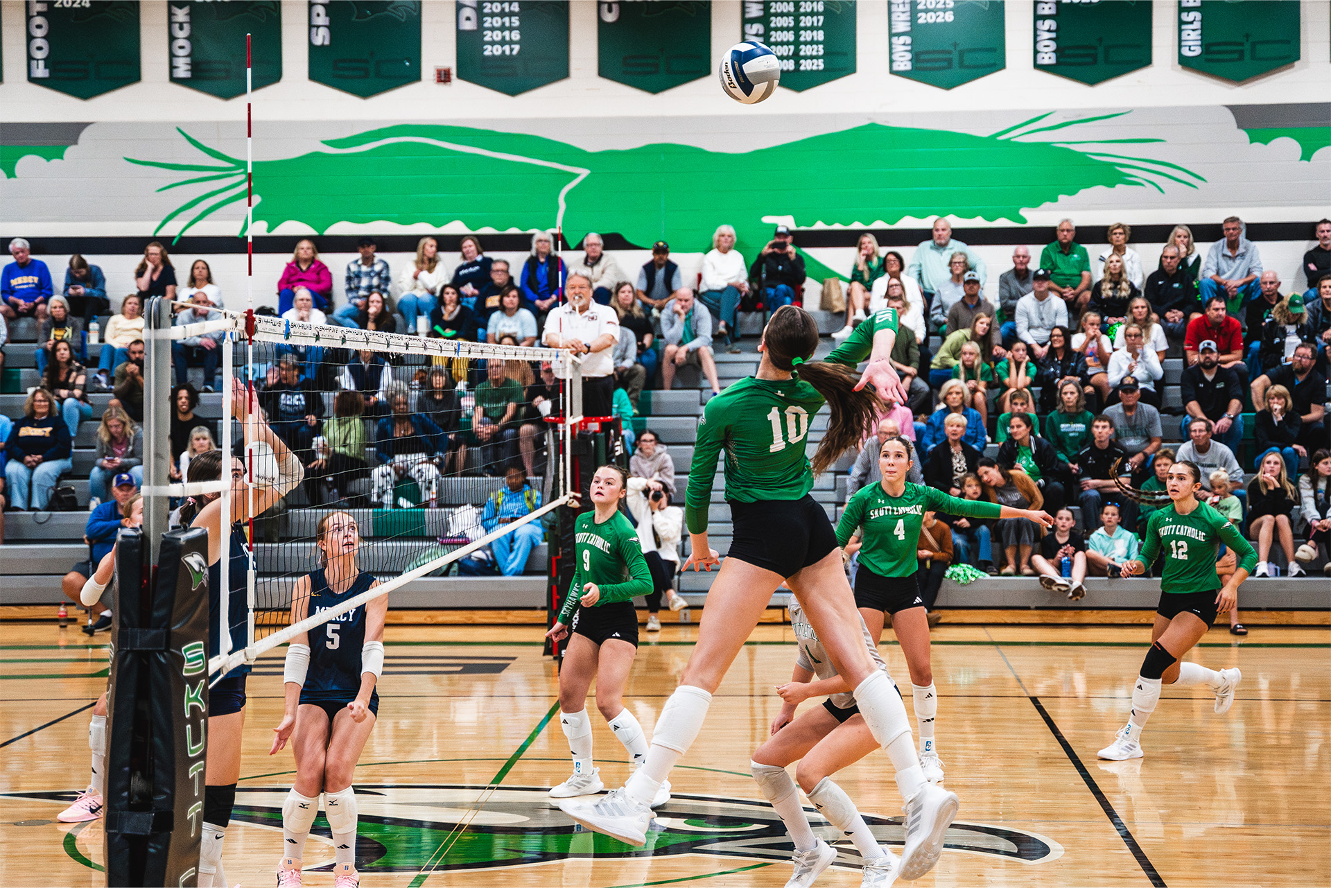 Skutt Catholic players track the ball as their teammate attacks at the net.